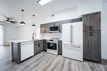 A modern kitchen with a white refrigerator, white countertops, and dark wood flooring.